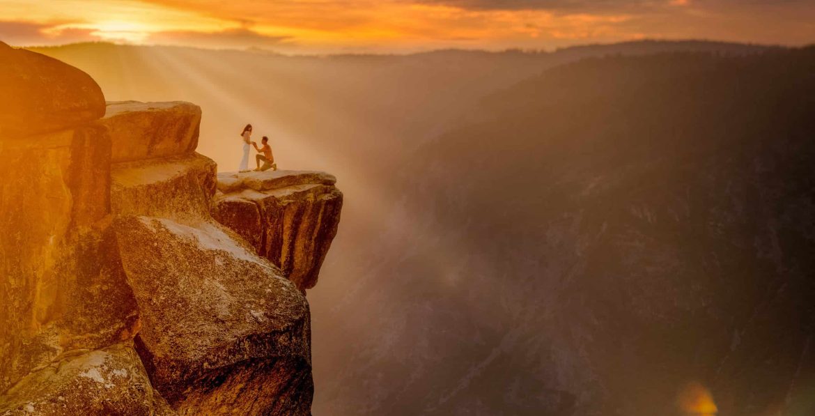 A couple standing on top of a cliff at sunset in yosemite national park.