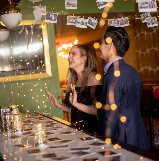 A couple at a bar with pictures hanging from the ceiling.