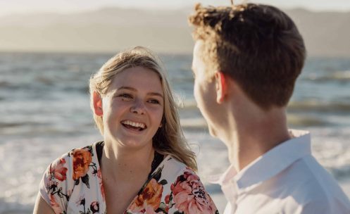 A couple laughing at the beach during their engagement session.