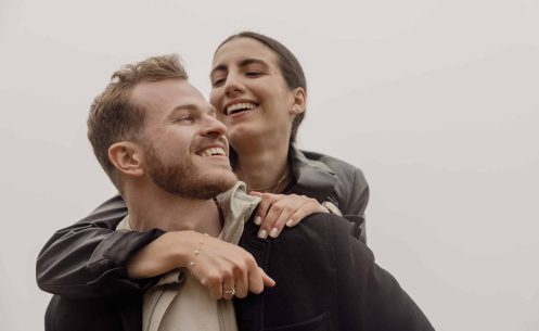 A man and a woman smiling while holding each other on a cloudy day.